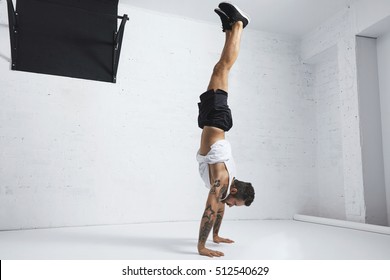 Strong tattooed in white unlabeled tank t-shirt male athlete shows calisthenic moves Handstand position