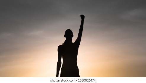 Strong, victorious , and motivated young woman raising her fist up to the sunset sky. Determination and overcoming adversity concept. - Shutterstock ID 1530026474