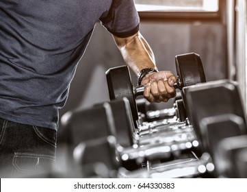 Strong well built bodybuilder lifting dumbbell weights getting ready for exercise in fitness