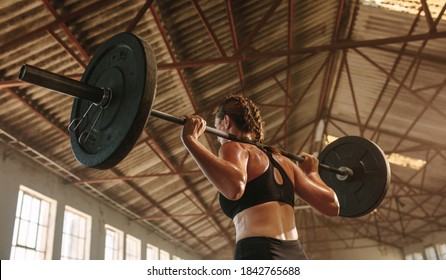 Strong woman exercising with barbell. Fit woman working out with heavy weights at cross training gym in factory shade. - Powered by Shutterstock