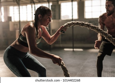 Strong woman exercising with battle ropes at the gym with male trainer. Athlete doing battle rope workout at gym with instructor. - Shutterstock ID 1014402268