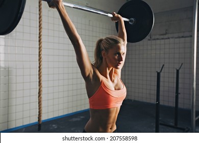 Strong woman lifting barbell as a part of crossfit exercise routine. Fit young woman lifting heavy weights at gym. - Powered by Shutterstock