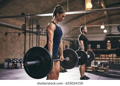 Strong woman and man holding heavy barbells in gym. Horizontal indoors shot - Powered by Shutterstock