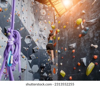 Strong woman on artificial climbing wall with colorful grips and ropes - Powered by Shutterstock