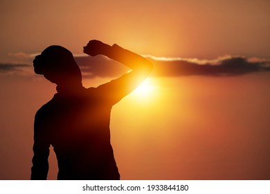 Strong woman raising her hands on sunset background