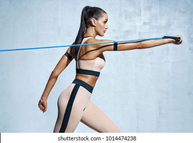 Strong Woman Using Resistance Band In Her Exercise Routine. Photo Of Fitness Model Workout On Grey Background. Strength And Motivation