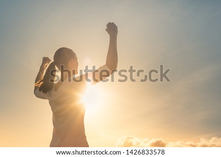 Strong woman, Winning, success , and life goals concept. Young woman with arms flexed facing the sunset. 