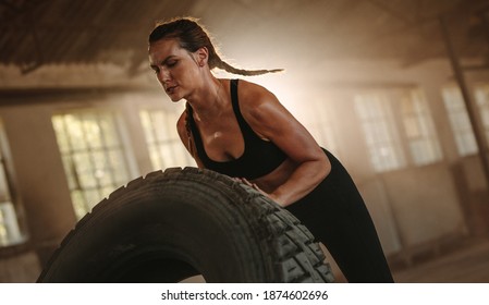 Strong woman working out with a huge tire in cross workout space. Woman exercising with big tire at an abandoned warehouse. - Powered by Shutterstock