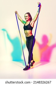Strong woman working with resistance band. Photo of woman in black sportswear on white background with effect of rgb colors shadows. Sports and healthy lifestyle
