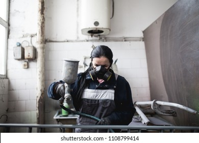 Strong And Worthy Woman Doing Hard Job. She Using Industrial Spray Compressor For Painting Some Metal Products.