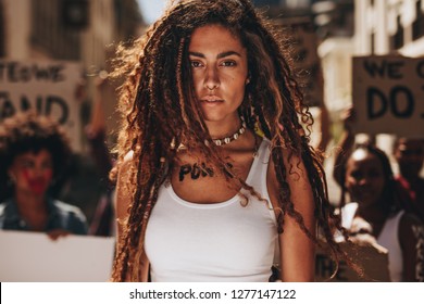 Strong Young Female Activist Protesting Outdoors With Group Of Women In Background. Woman With Word Power Written On Her Body.