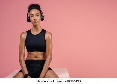 Strong young female athlete in sportswear and headphones sitting on box. African woman in sportswear relaxing after fitness training session. - Powered by Shutterstock