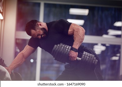 strong young man with beard wearing black sport clothes lifting heavy weight dumbbell with on hand training back in gym workout - Powered by Shutterstock