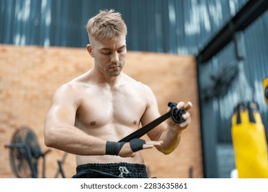 Strong young man boxer wrapping his fists and hands with black bandage tape before boxing fight and training in fitness gym. Athlete doing workout - Powered by Shutterstock