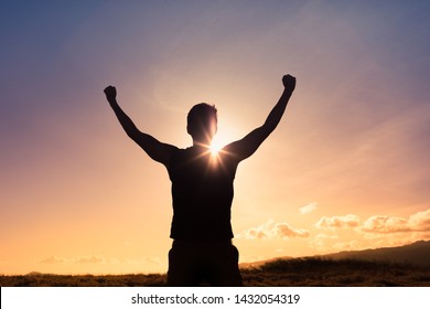 Strong young man with fist in the air standing on top a mountain. Triumph, victory and feeling determined.
