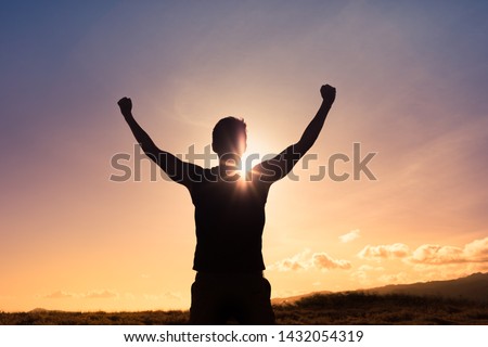 Strong young man with fist in the air standing on top a mountain. Triumph, victory and feeling determined.