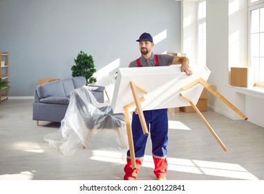 Strong Young Man From A Moving Company Or Truck Delivery Service Carrying A White Wooden Table While Removing Furniture From A Modern House Or Apartment