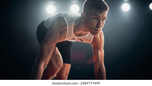 Strong Young Man Starting a Race From Track Starting Blocks Position on a Dark Stadium in the Evening. Portrait of a Fit Male Sprint Runner Participating for an International Competition - Powered by Shutterstock