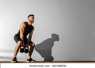 Un hombre fuerte y joven centrado en la musculatura, con músculos grandes sosteniendo campanas pesadas