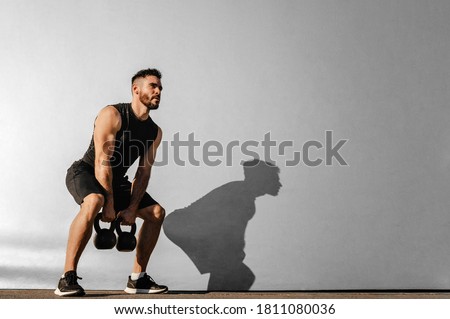 Strong young muscular focused fit man with big muscles holding heavy kettlebells