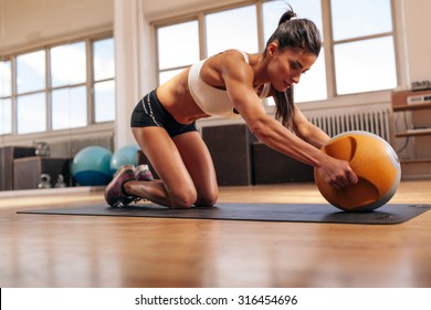Strong young woman doing intense workout with kettlebell in gym. Young muscular woman doing core exercise on fitness mat in health club.