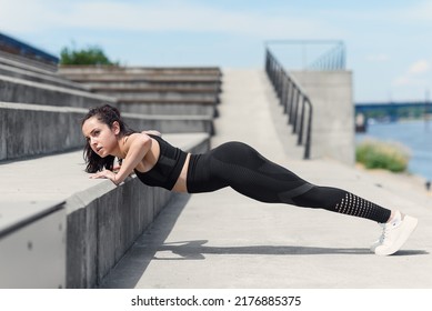 Strong young woman doing push ups on steps outdoors. Sportswoman doing push ups exercises in morning.