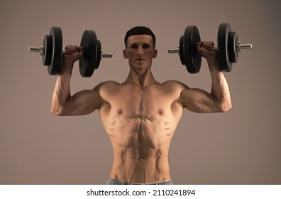 Strongman with muscular torso lift dumbbells in strong arms biceps triceps grey background, strength