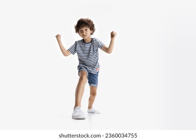 Strongman. One curly Caucasian preschool boy in casual clothing with hands up posing isolated on white studio background. Copyspace for ad