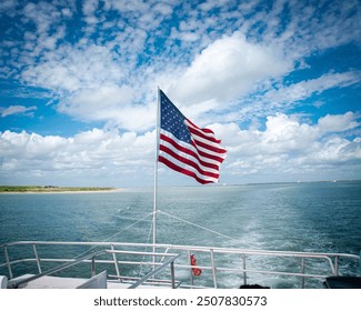 Strongwater splashed from stern of boat cruise tour with proudly display American flag flying under sunny cloud blue sky in South Padre Island, Independence Day patriotism theme, red blue white. USA
