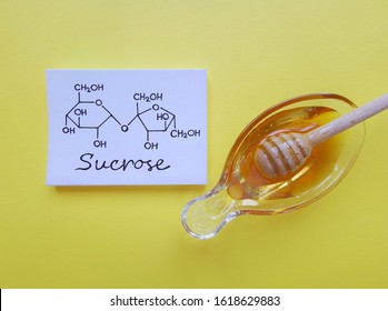Structural chemical formula of sucrose molecule with a bowl of honey. It is a disaccharide molecule composed of glucose and fructose. Honey gets its sweetness from fructose, glucose, and sucrose.