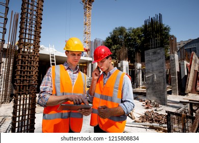 Structural engineer and architect dressed in orange work vests and  hard hats discuss the construction process by the phone and use tablet  on the open building site