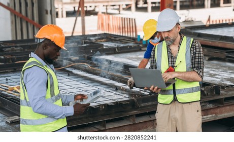 Structural engineer and foreman worker using a digital touch pad to discuss and plan construction workflows at an outdoor building site.