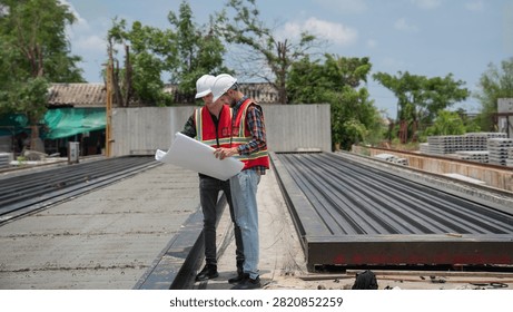 Structural engineer and foreman worker using a digital touch pad to discuss and plan construction workflows at an outdoor building site.