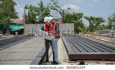 Structural engineer and foreman worker using a digital touch pad to discuss and plan construction workflows at an outdoor building site.