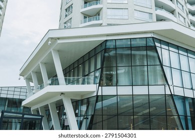 A structure features a glass front with geometric shapes and open spaces. It stands tall among other buildings in a busy urban environment during the day.