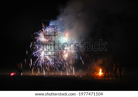 Structure with pyrotechnics and fireworks exploding and sparks during a celebratory night. People looking for a firework display with a bonfire during new years. Festival and celebration.