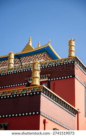 The structure of a Tibetan temple rises under a clear blue sky, showcasing vibrant colors, detailed designs, and traditional elements typical of Buddhist architecture.