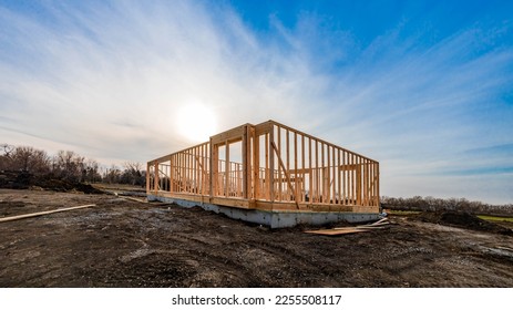 The structure of wood framing at construction site against a vast cloudy sky with bright sun behind. New build home at empty lot. framework ready for wall and roof install. Real estate development. - Shutterstock ID 2255508117