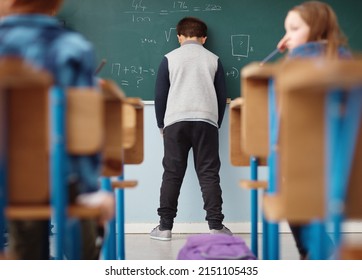 Struggling at school. Rear view shot of an elementary school boy leaning with his head on the chalkboard in class.
