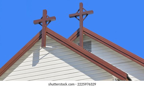 St.Saviour's Chruch rear facade with triangular pediment of white painted, horizontal wooden slats and brown colored double cross on rooftop against a clear blue sky. Kuranda-Queensland-Australia.