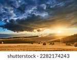 Stubble in a field with bales under a spectacular sky with clouds through which the sun