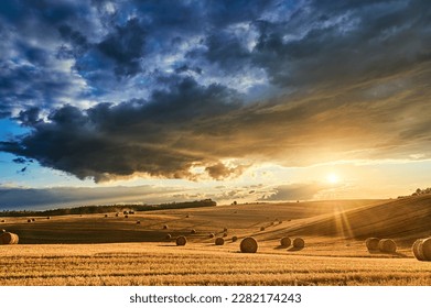 Stubble in a field with bales under a spectacular sky with clouds through which the sun's rays shine through - Powered by Shutterstock