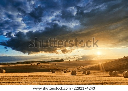 Stubble in a field with bales under a spectacular sky with clouds through which the sun's rays shine through
