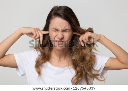 Stubborn annoyed woman sticking plug fingers in ears not listening to loud noise sound isolated on white blank studio background, young angry teen refuse hear avoid stress feel ear pain ache concept