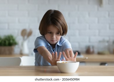 Stubborn little kid boy rejecting eating dry breakfast corn flakes with milk, sitting in kitchen without appetite. Upset small male child does not want eating tasteless food, loss of appetite.