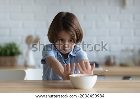 Stubborn little kid boy rejecting eating dry breakfast corn flakes with milk, sitting in kitchen without appetite. Upset small male child does not want eating tasteless food, loss of appetite.