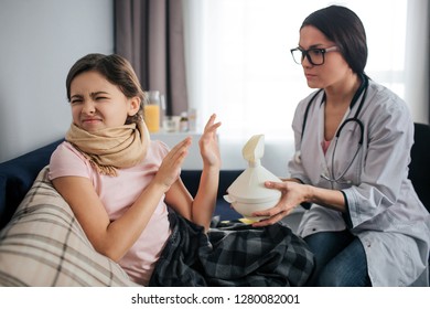 Stubborn Sick Girl Shrink And Keep Eyes Closed. She Doesn't Want To Do Inhalation Procedure. Female Doctor Hold White Inhaler And Give It To Kid. They Sit In One Room.