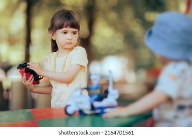 
Stubborn Toddler Child Refusing to Share Toy with Her Brother. Siblings fighting over toys playing together outdoors
