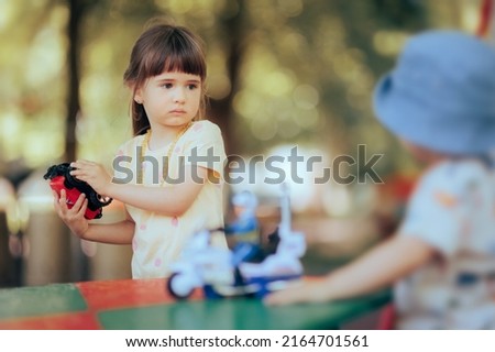 
Stubborn Toddler Child Refusing to Share Toy with Her Brother. Siblings fighting over toys playing together outdoors
