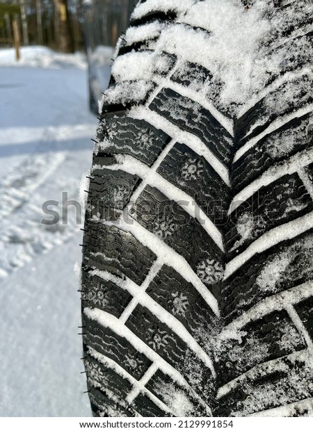 Studded winter tire on light snow. Sunny winter day\
with brand new winter tires. Snowy ground. Winter transportation\
concept image. Closeup\
image